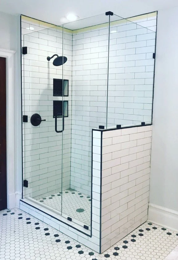 A modern shower with glass walls and black fixtures, tiled with white subway tiles, and black and white hexagon floor tiles.