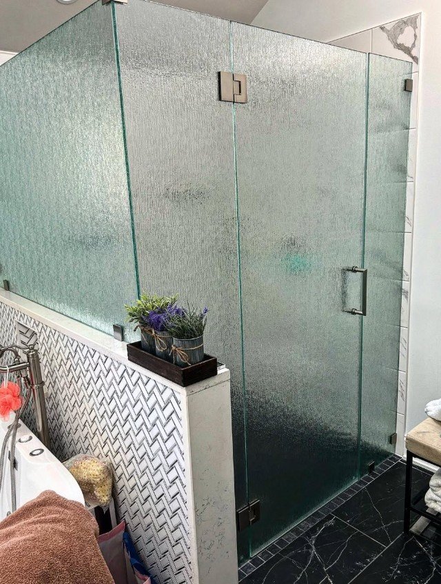 Glass shower enclosure in a bathroom with black tiled floor and decorative white wall pattern.