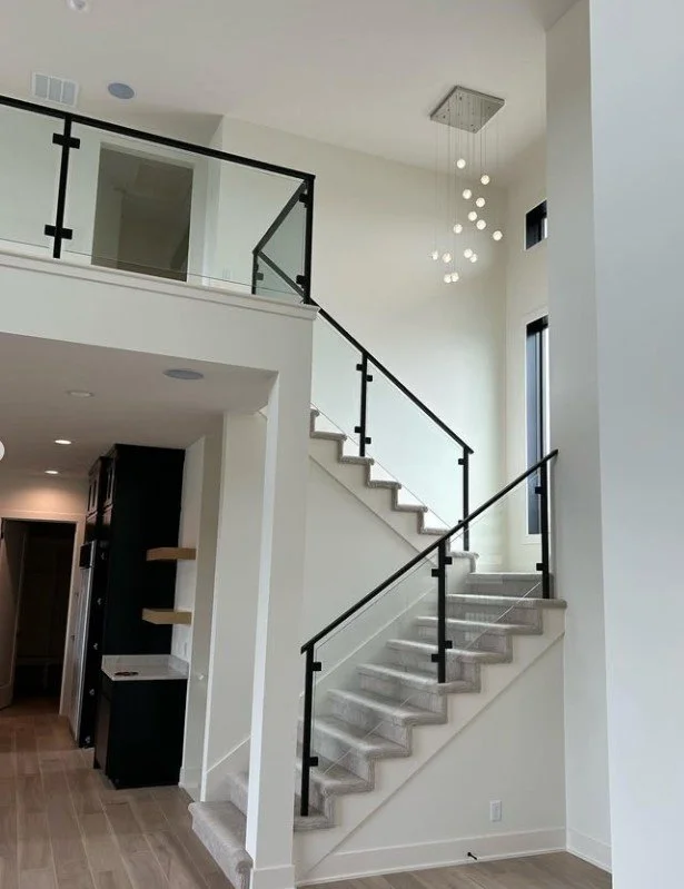 Modern staircase inside a bright home with black metal railings, light-colored steps, and contemporary hanging light fixtures.