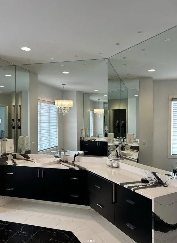 Modern bathroom with a large, multi-sectioned mirror wall, a white marble countertop with black cabinetry, a sink, and a chandelier with hanging crystals.