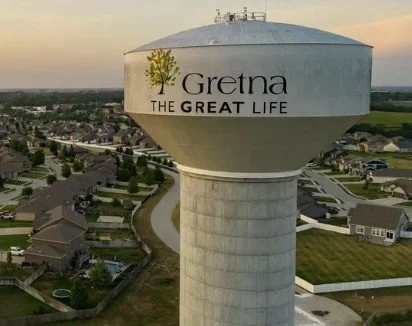 Water tower with 'Gretna The Great Life' written on it, surrounded by suburban houses.