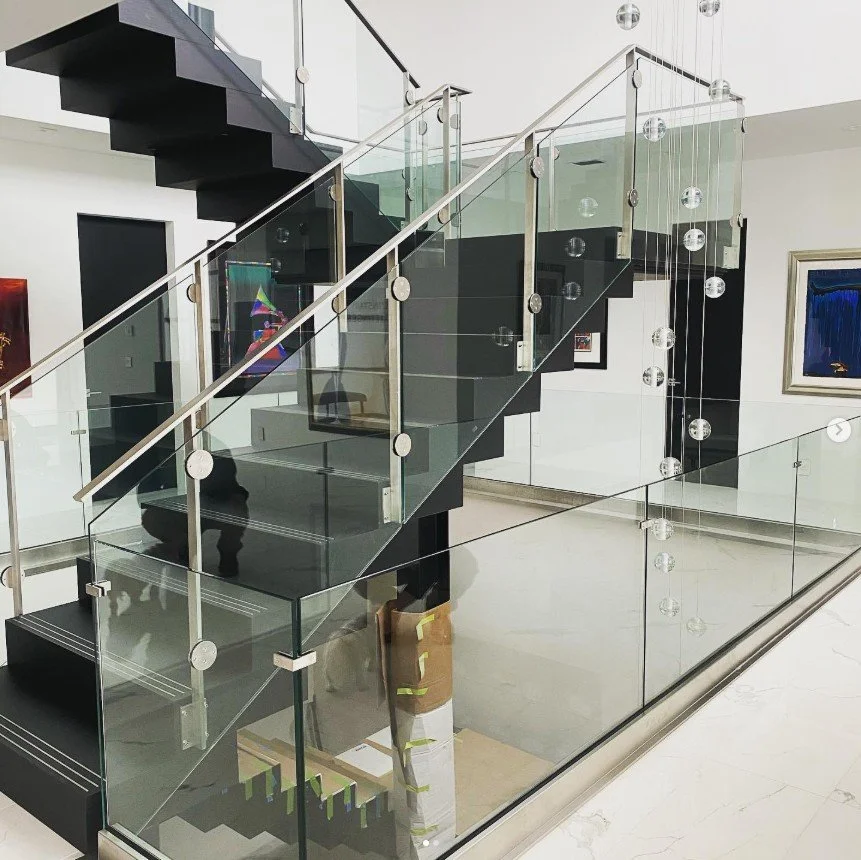 Modern staircase with black steps, glass railing, and decorative hanging glass spheres in a contemporary art gallery or home interior.