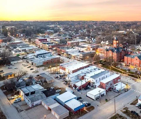 Aerial view of a small town at sunset, showcasing a mix of commercial buildings, warehouses, and a church with a clock tower.