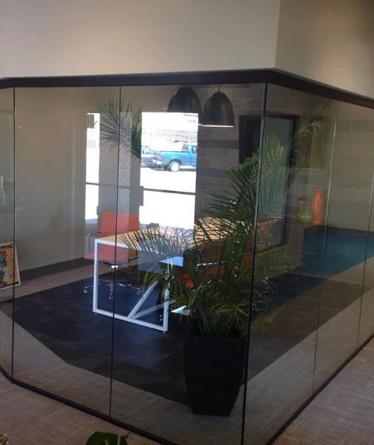 Indoor modern office or waiting area with glass walls, orange chair, white table, and large potted plant.