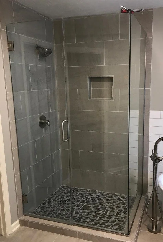 Walk-in shower with gray tiles, a glass door, built-in shelf, and a black and gray mosaic tile shower floor.