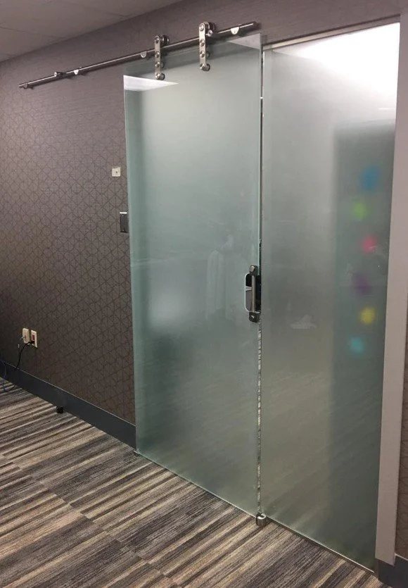 Frosted glass sliding door on a modern office wall with a patterned wall behind it and a carpeted floor.