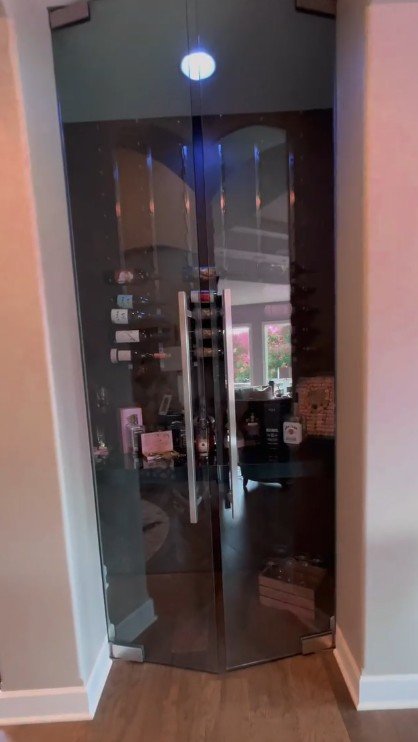 Glass door with vertical metal handles and a reflection showing a room with a window and shelves.