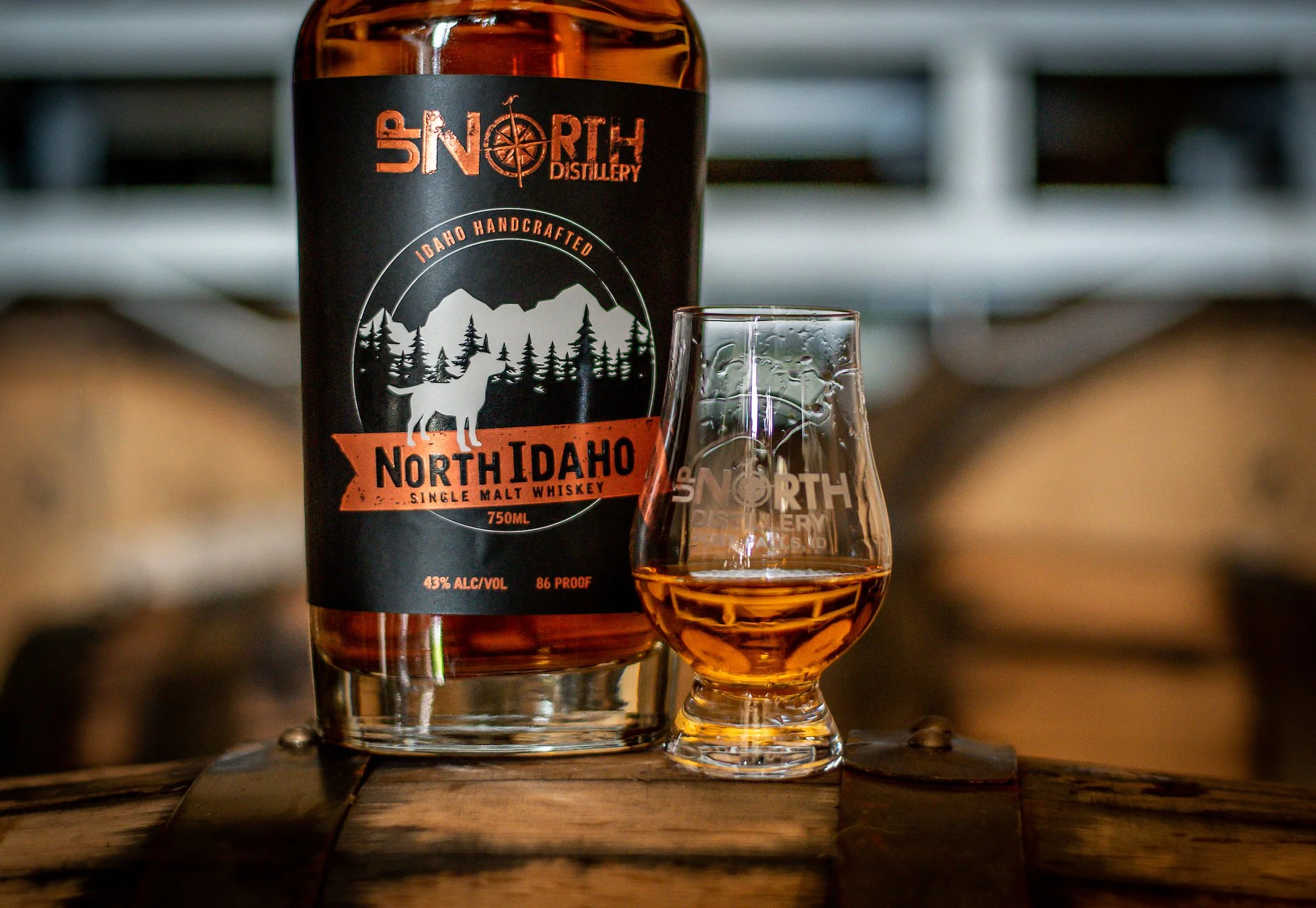 A bottle of North Idaho single malt whiskey and a whiskey glass filled with amber whiskey on a wooden surface.