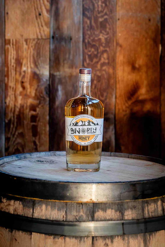 A bottle of honey whiskey on top of a wooden barrel with a wooden wall background.