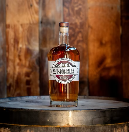 A clear glass bottle of North Disillery brandy on a wooden barrel, with a wooden background.