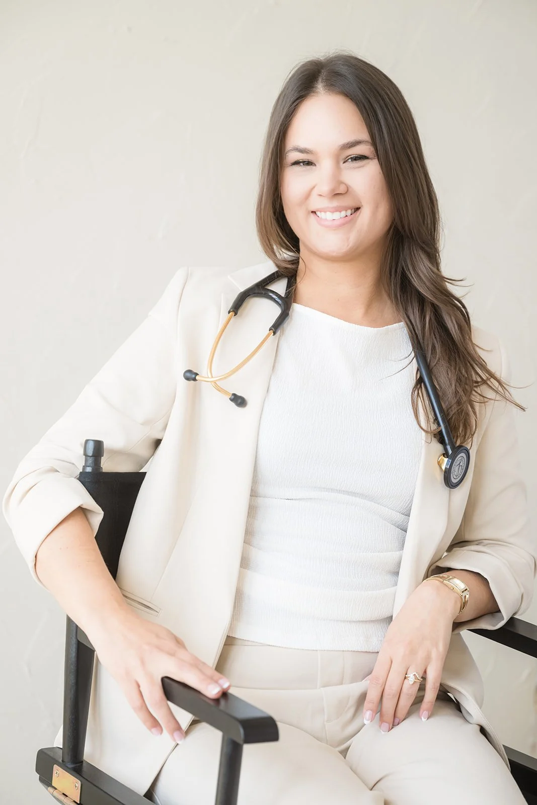 Smiling female doctor sitting in a wheelchair with a stethoscope around her neck, wearing a white blazer and cream-colored outfit.