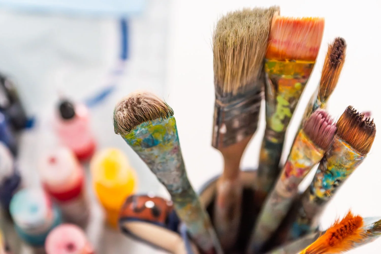 Collection of artist paintbrushes with colorful paint and bristles, placed in a holder.