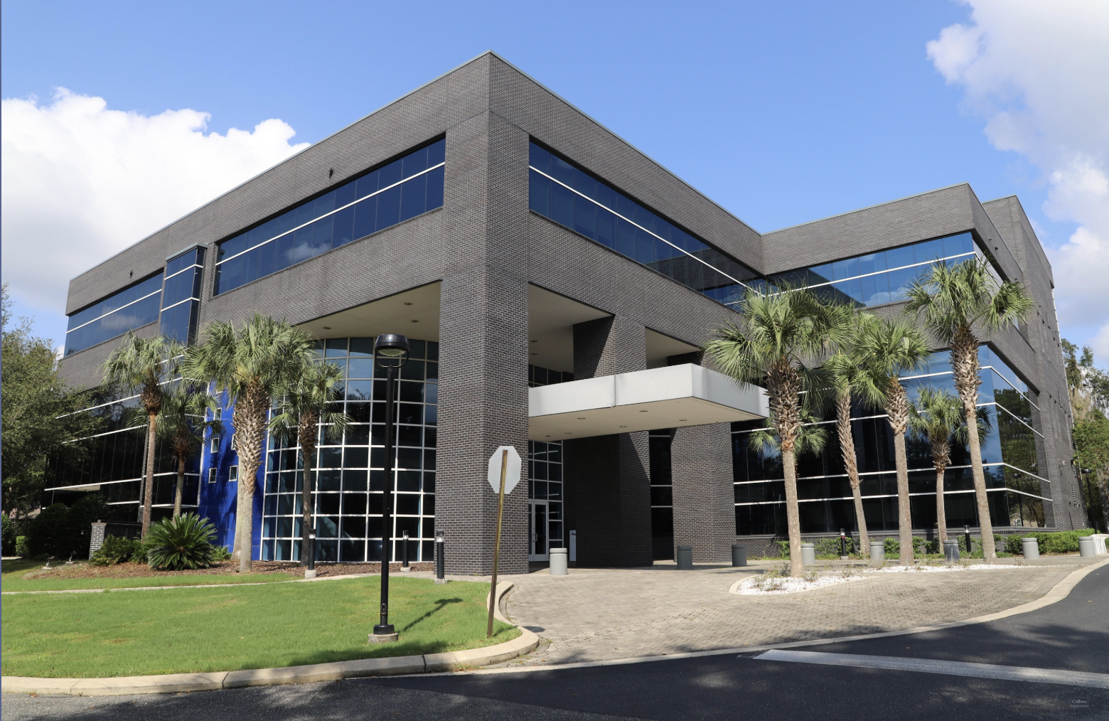 Modern office building with glass windows surrounded by palm trees under a partly cloudy sky.