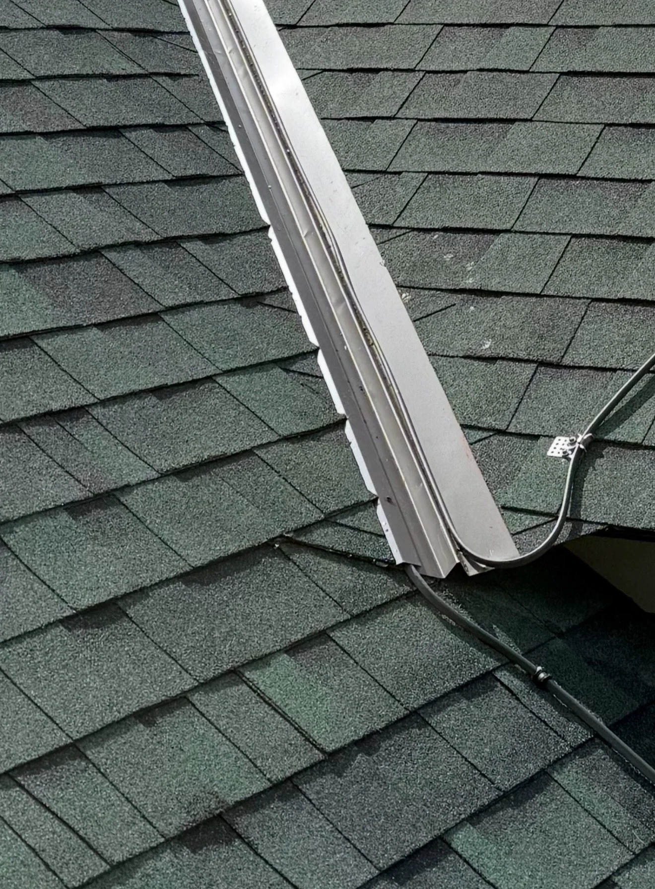 Heat trace cable routed under a metal valley cover on a dark asphalt shingle roof