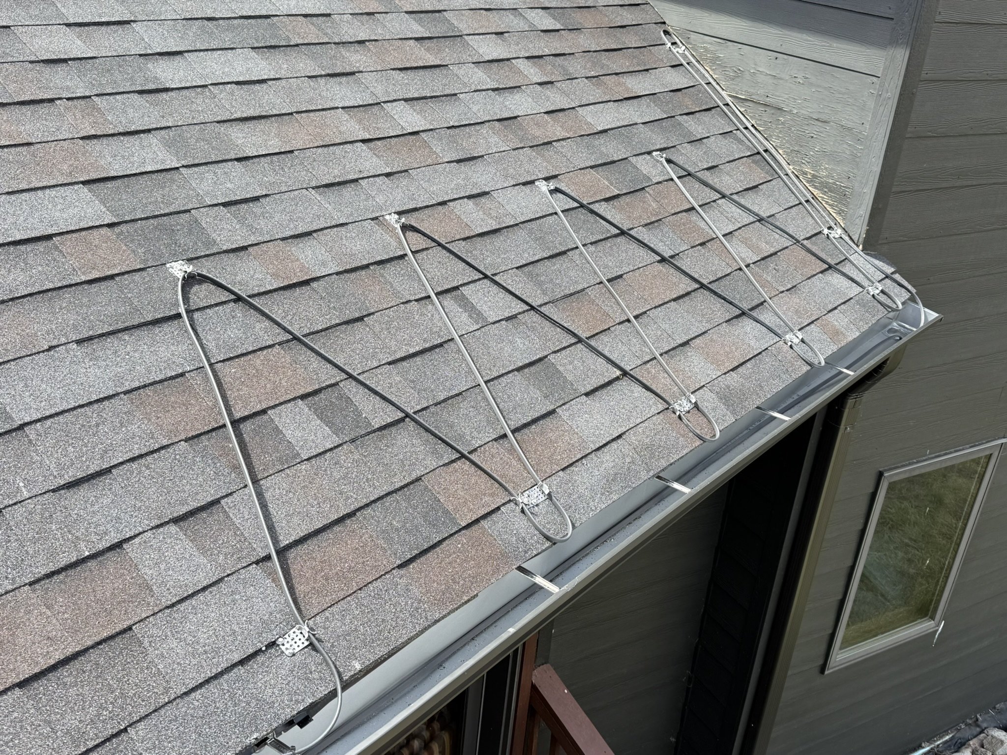 Heat trace cable clipped in loops along a shingle roof edge above the gutter