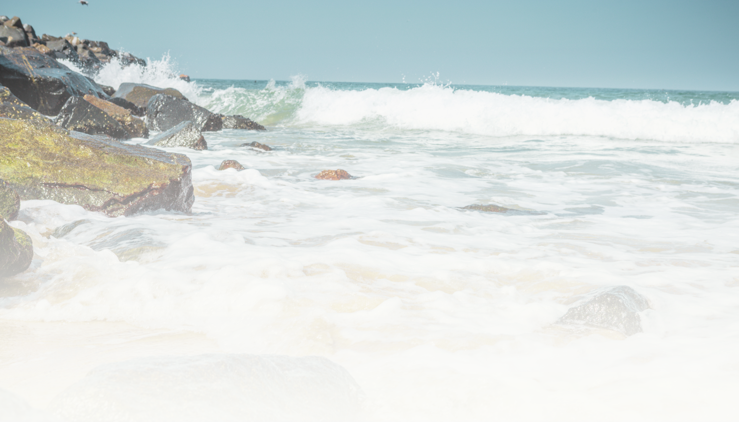 Ocean waves crashing against rocks on a sandy beach.