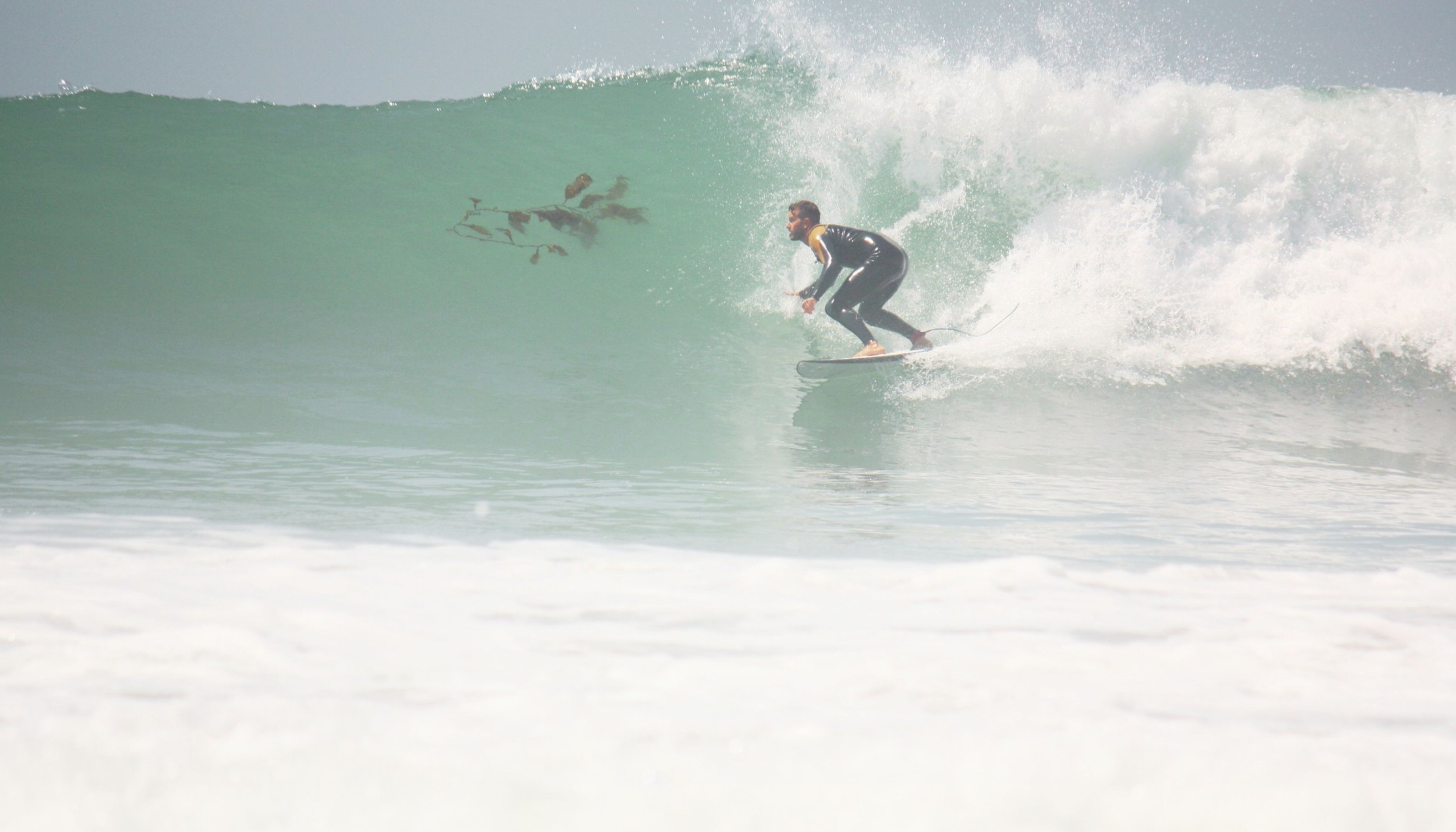 A surfer wearing a black wetsuit riding a wave with spray in the air, close to the shore.