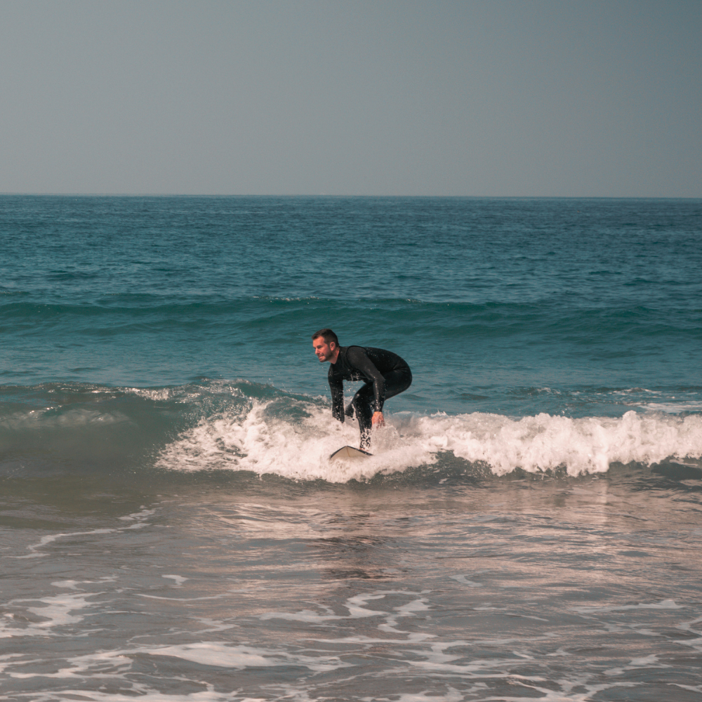A man in a black wetsuit riding a small wave at the beach.