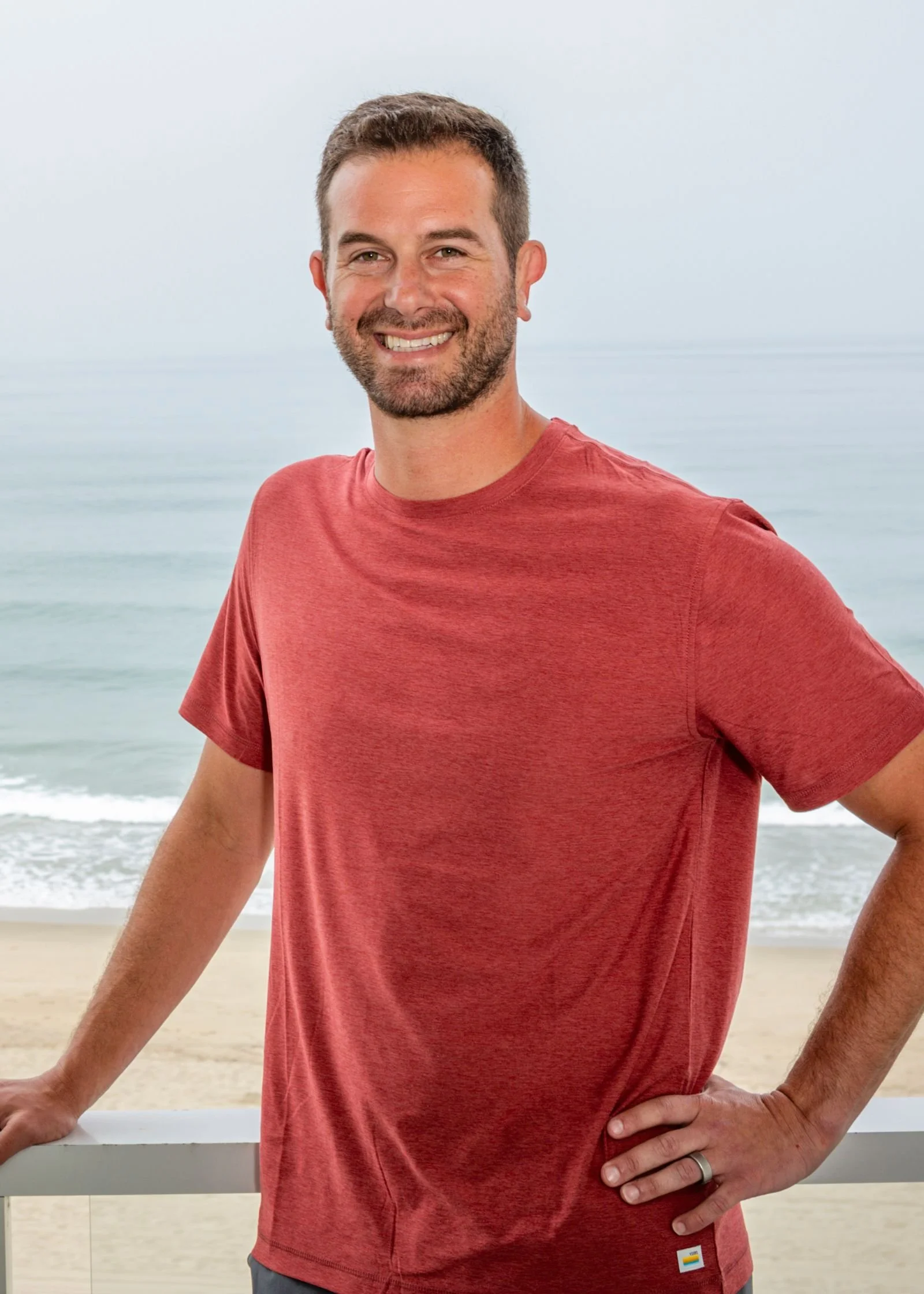 Joseph Sparks, LCSW, founder of Sparking Change Wellness, smiling on a balcony above the beach in a red t-shirt.