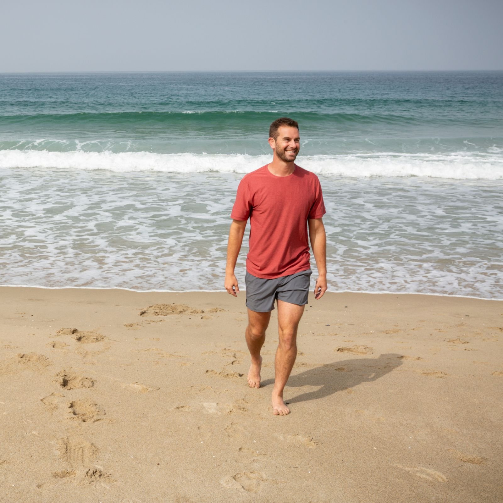 Joseph Sparks walking barefoot on the beach near the ocean waves.