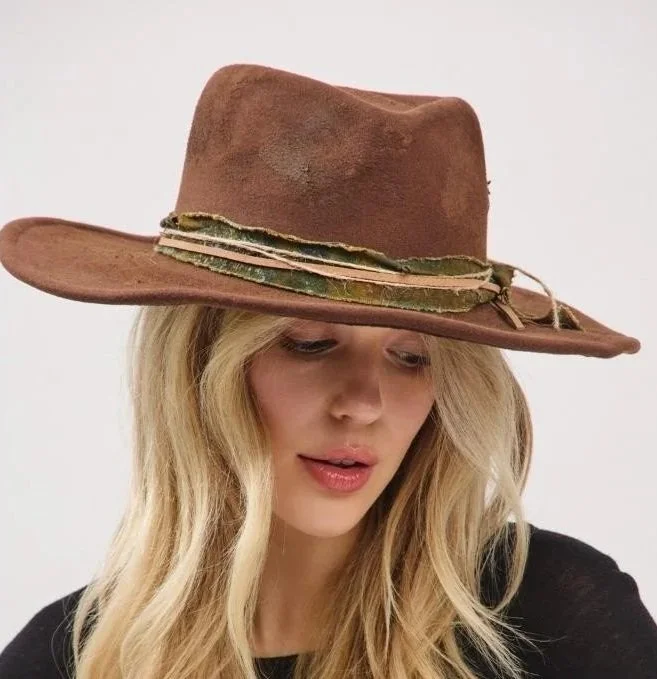 Woman with long blonde hair wearing a wide-brimmed brown felt hat with a decorative band.