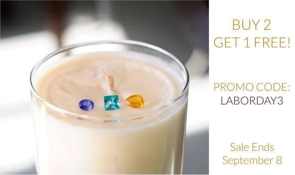 A glass of candle with small colored stones on top, alongside promotional text about a buy two get one free deal with a promo code 'LABORDAY3', ending September 8.