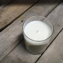 A white candle in a clear glass container placed on a wooden surface.