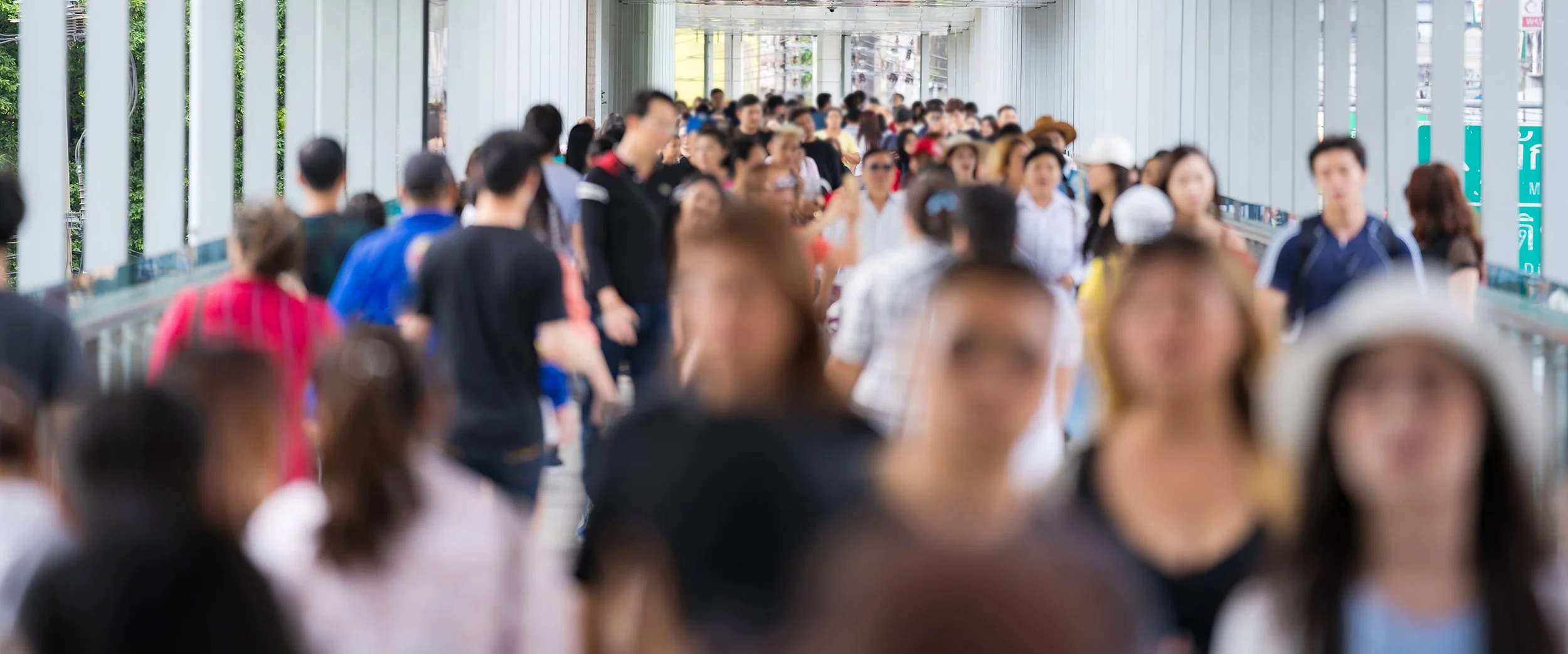 Crowded walkway with many people walking in both directions under a covered passageway.