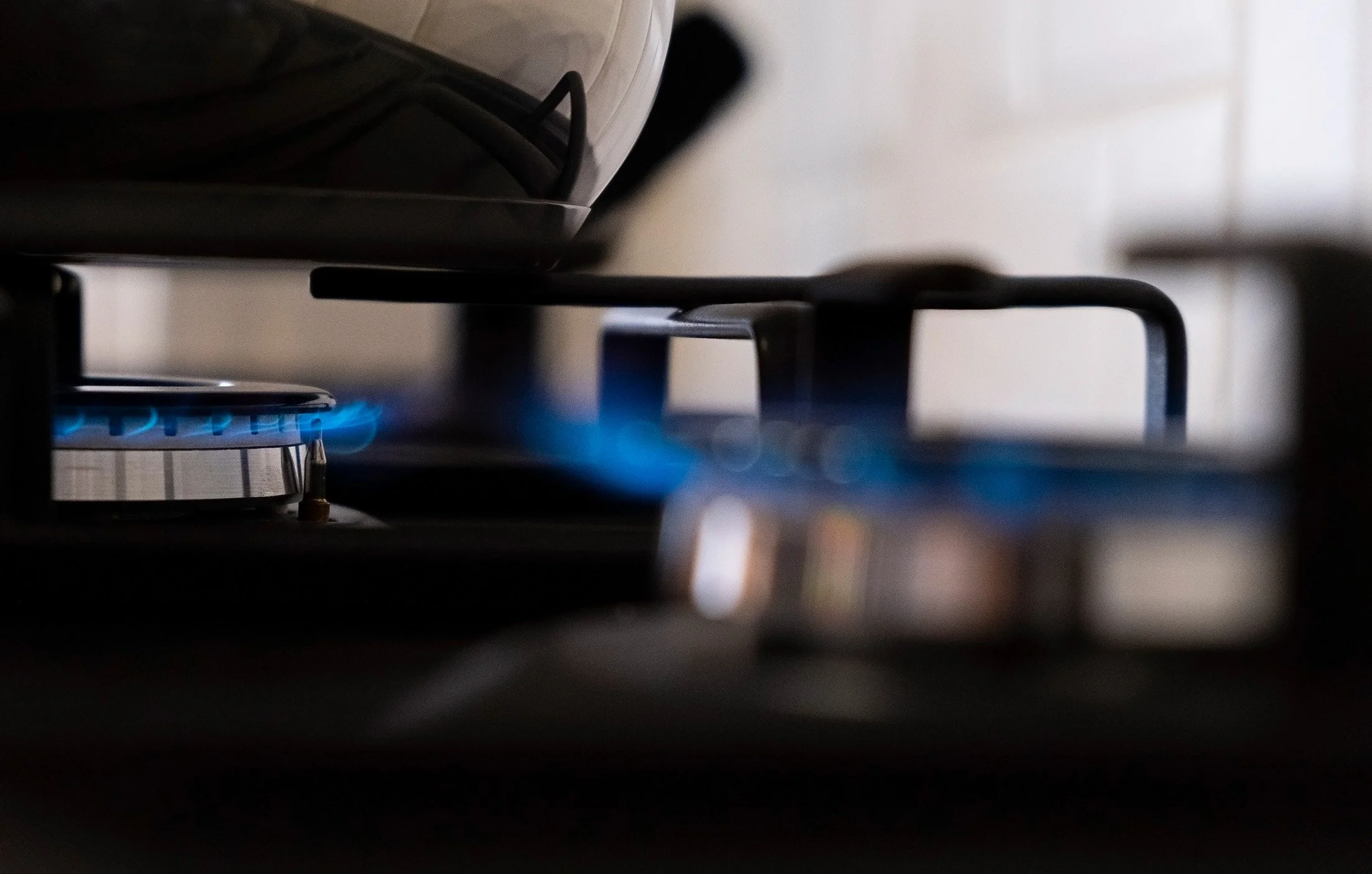 Close-up of a gas stove with blue flames under a pot, showing part of the stovetop and flame, with a blurred background.