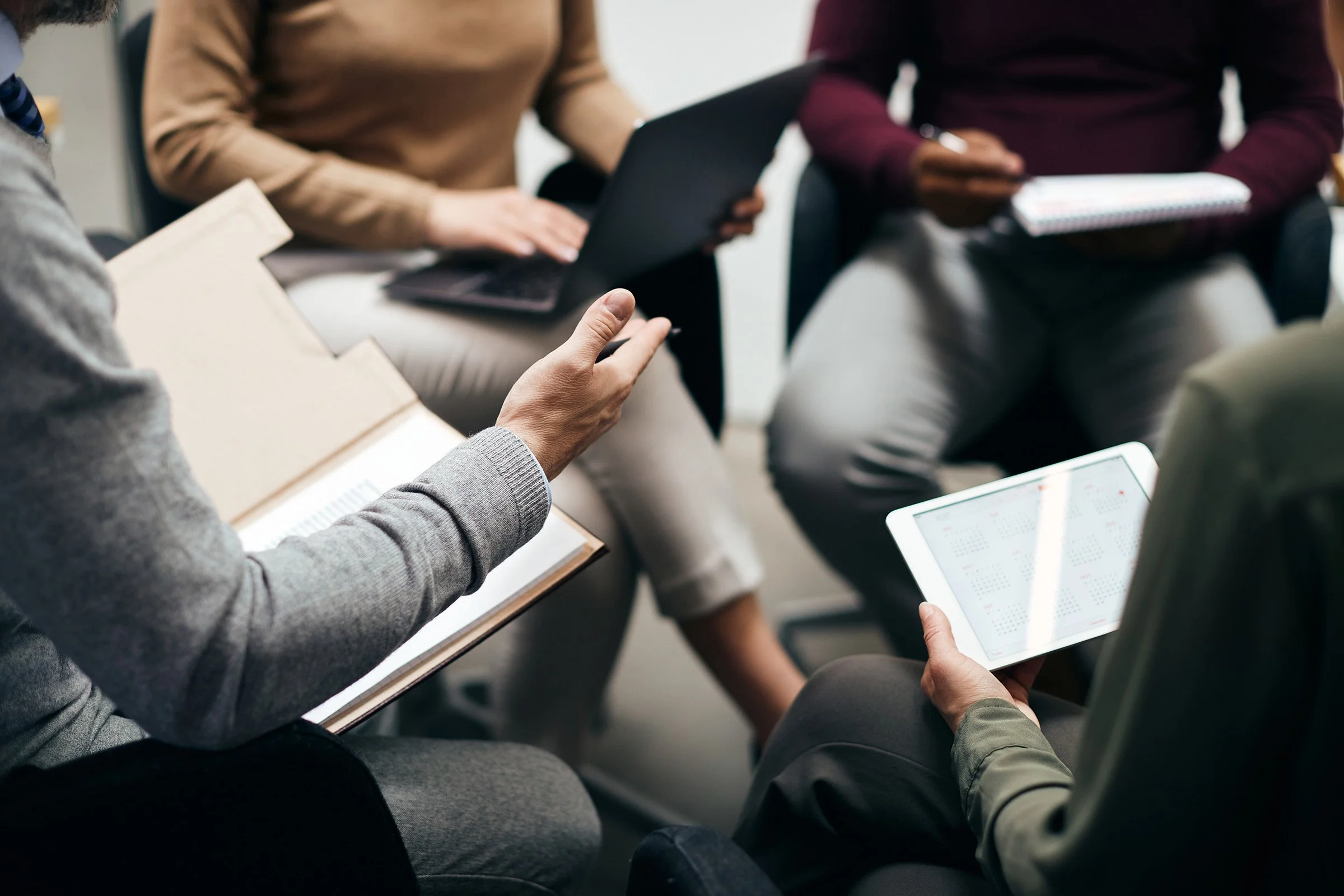 Group of people sitting in a meeting, holding tablets and notebooks.