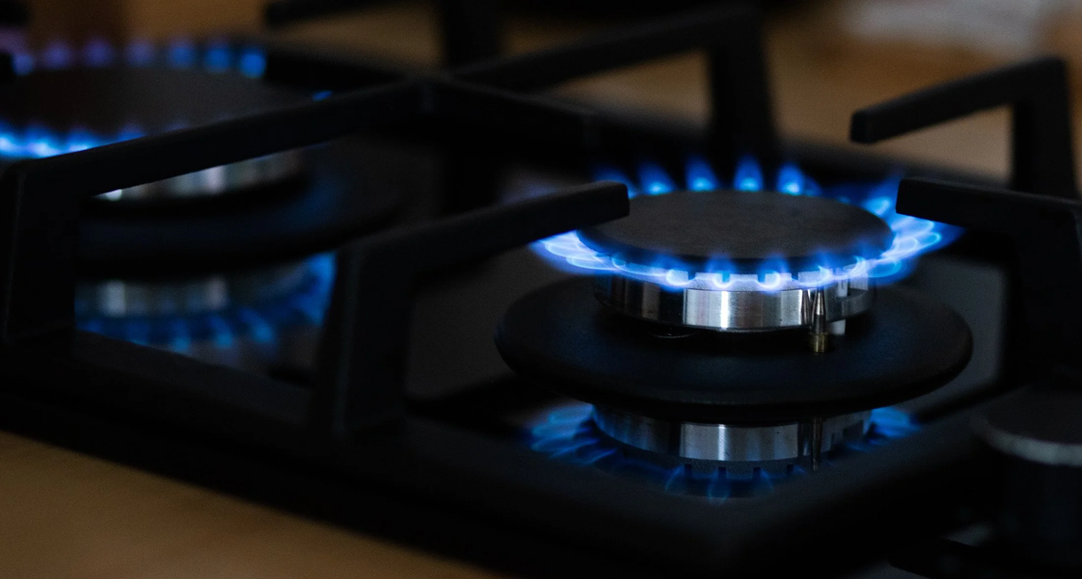 Close-up of a lit blue gas burner on a stove with the flames visible.