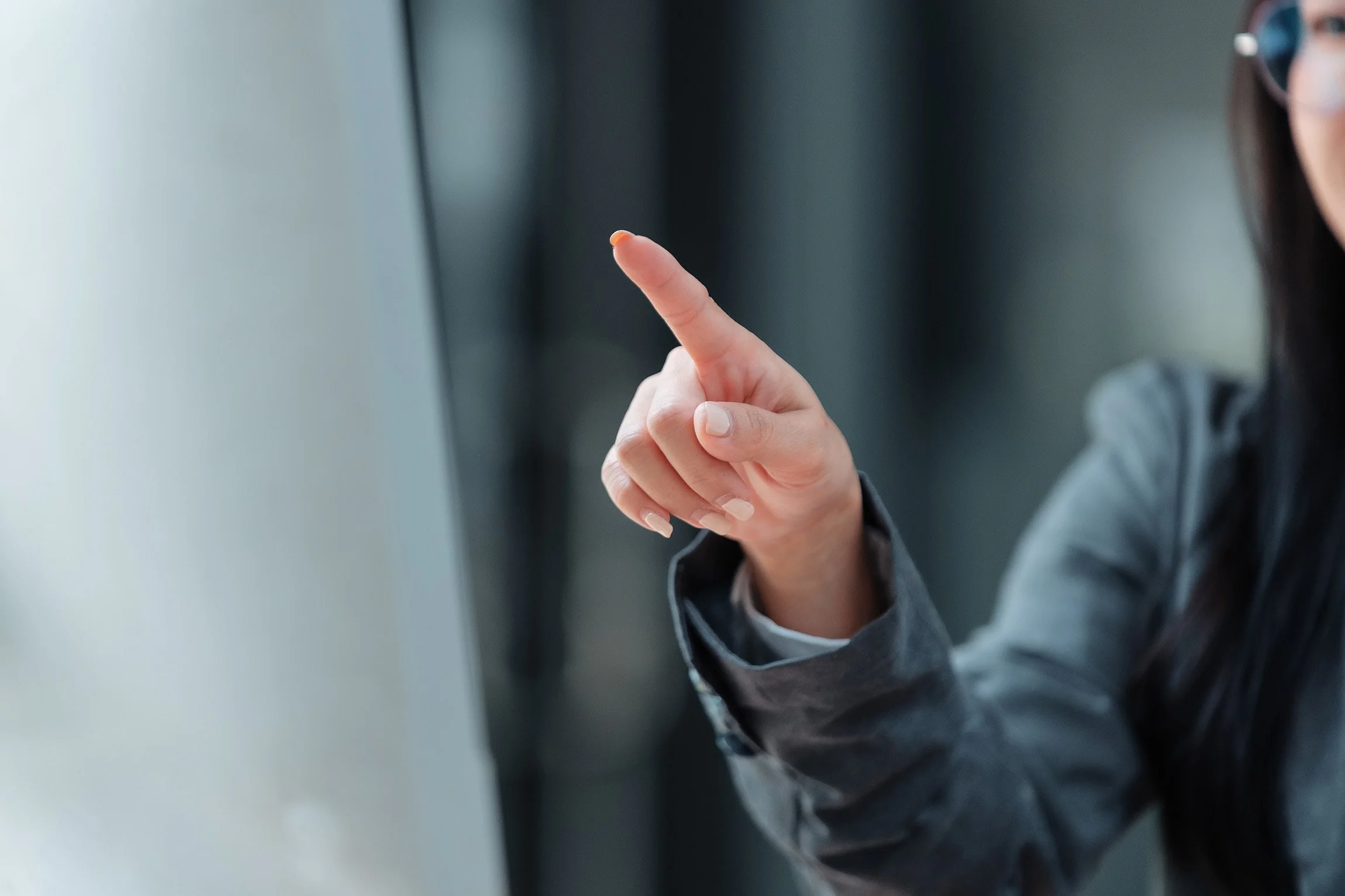 A person in a gray blazer pointing with their index finger.