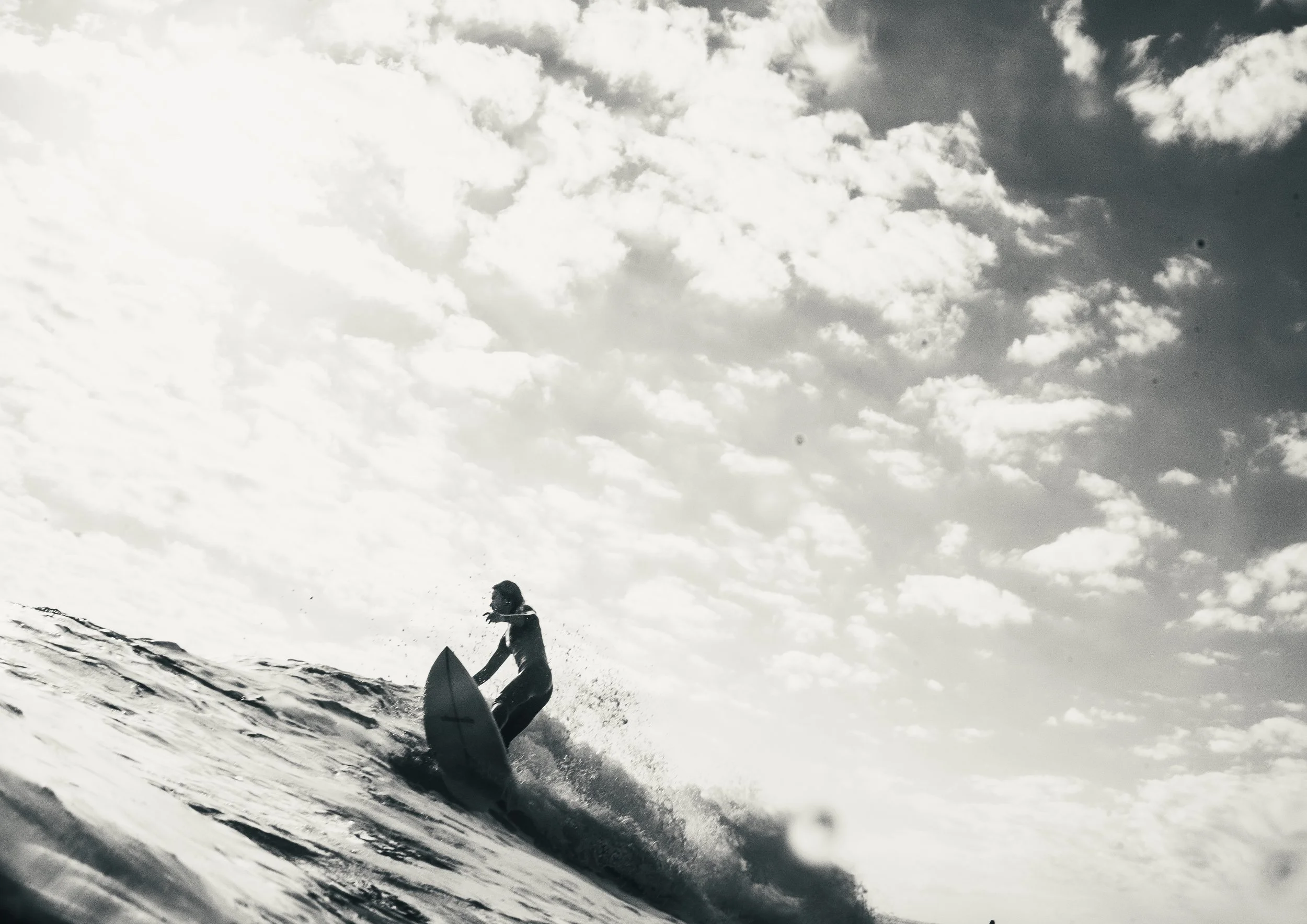 A person surfing on a wave in the ocean under a cloudy sky, black and white photograph.