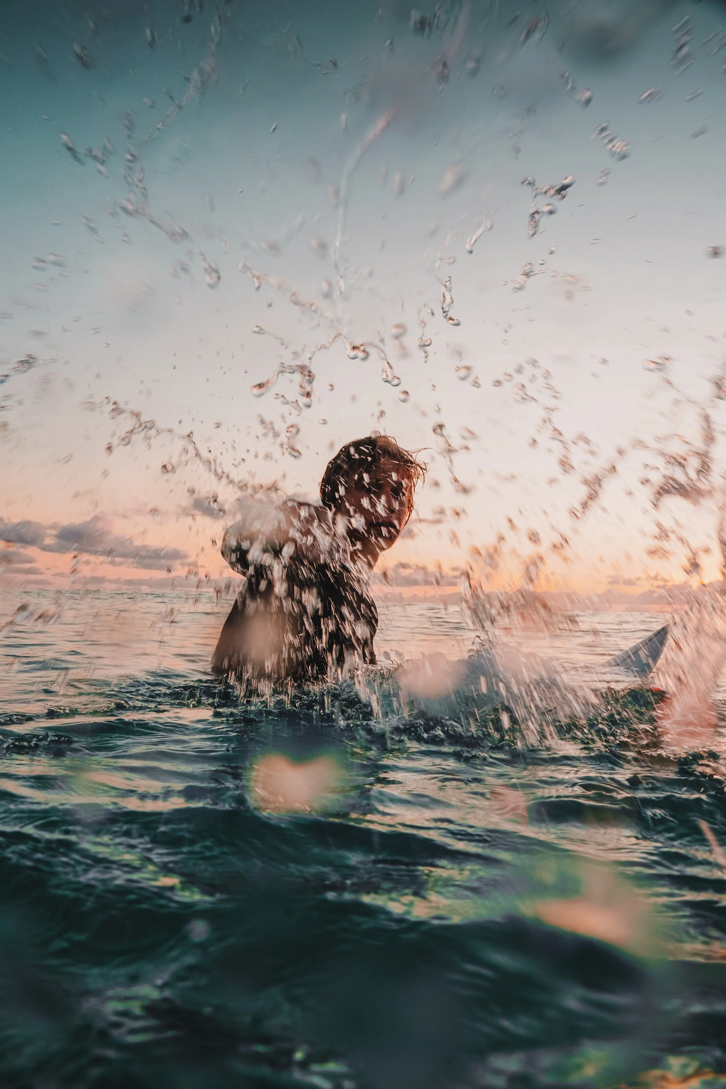 Person splashing water in the ocean during sunset.