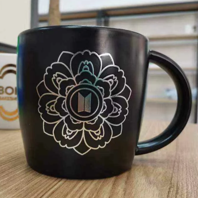 Black coffee mug with a white floral design and a logo in the center, placed on a wooden surface.