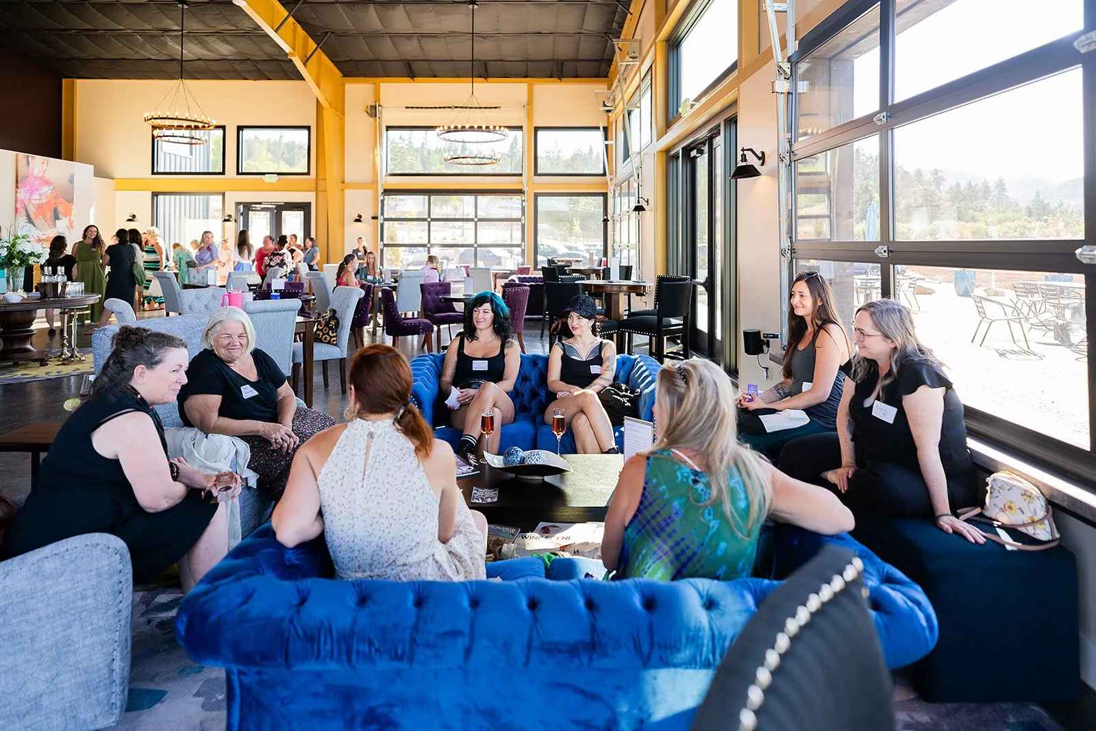 Group of women sitting on colorful couches and chairs in a bright, spacious indoor venue in Jacksonville, OR for Rogue Valley Women in Business.