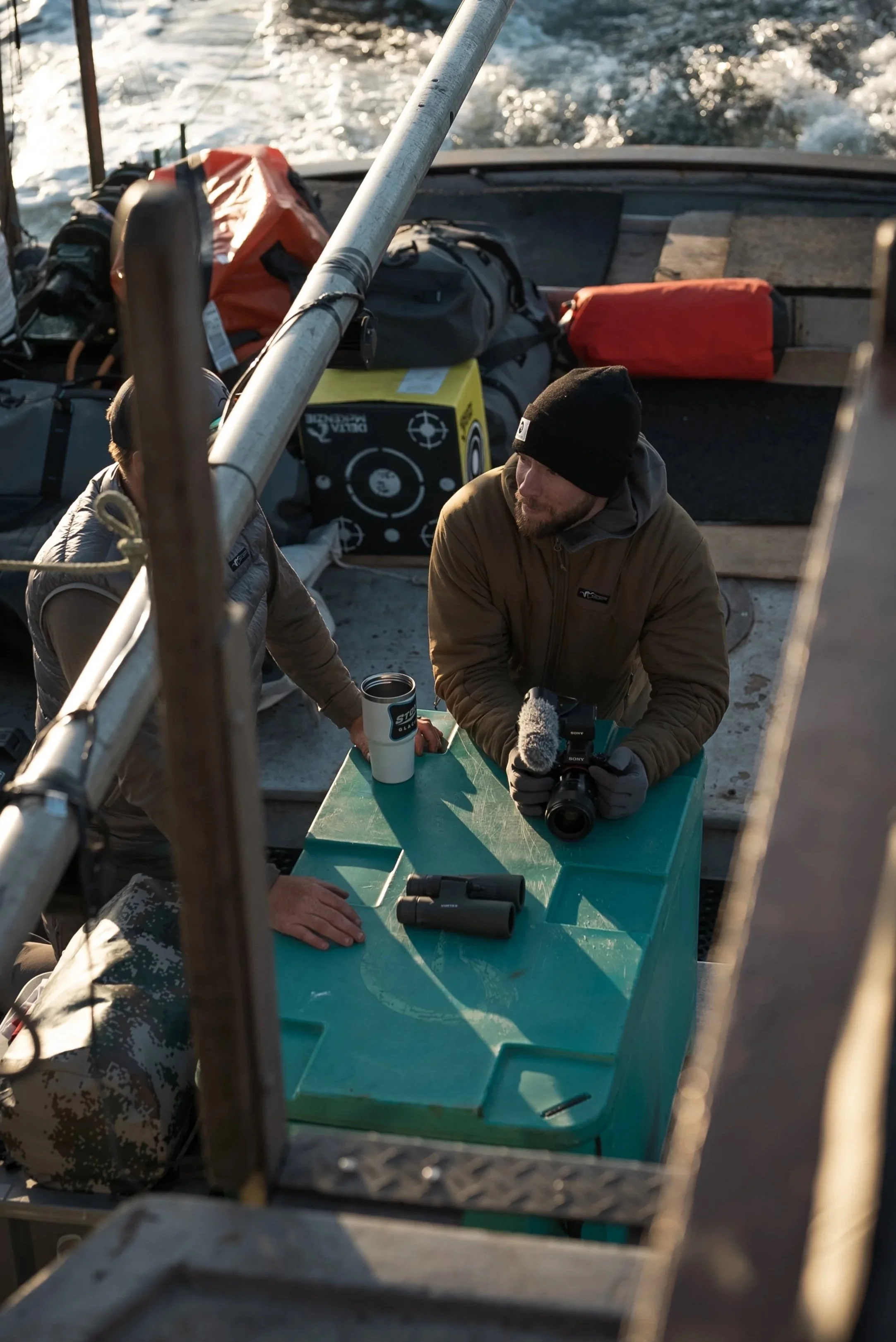Two men on a boat with equipment, one holding a Sony a1, with the ocean in the background.