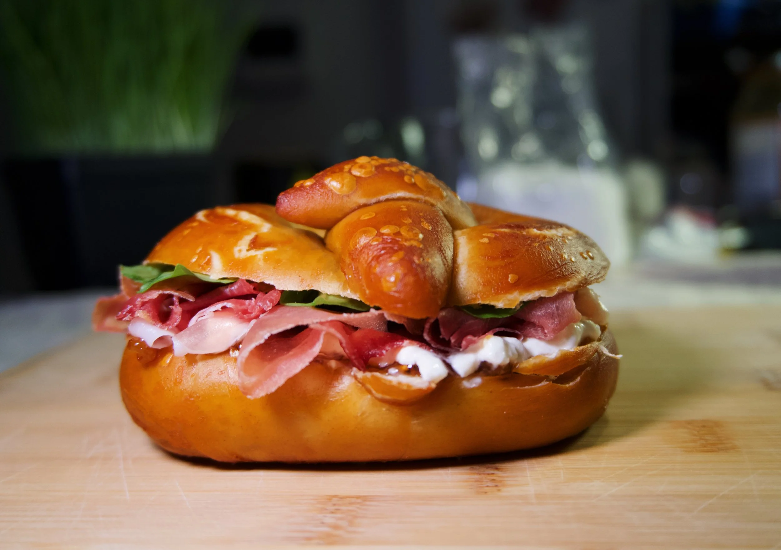 Sandwich with layers of sliced ham, lettuce, and cheese in a golden bun, topped with a pretzel roll.