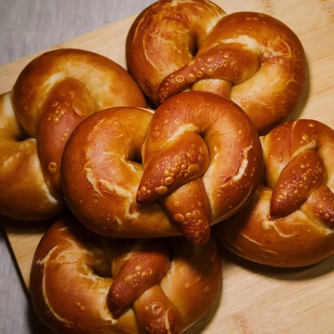 Freshly baked pretzels with a golden-brown crust on a wooden cutting board.