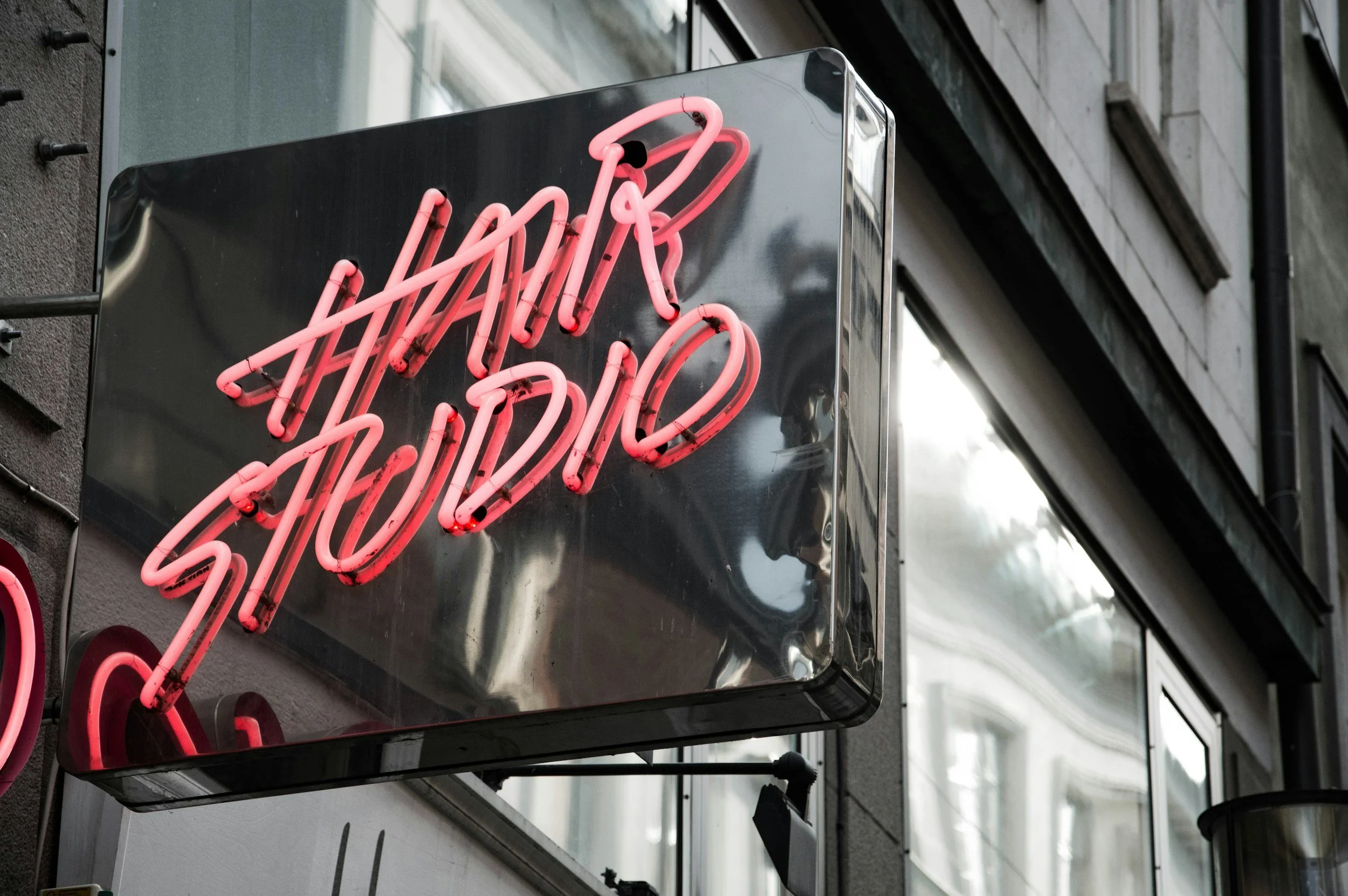 Pink neon sign reading 'Open' on a black rectangular background outside a building.