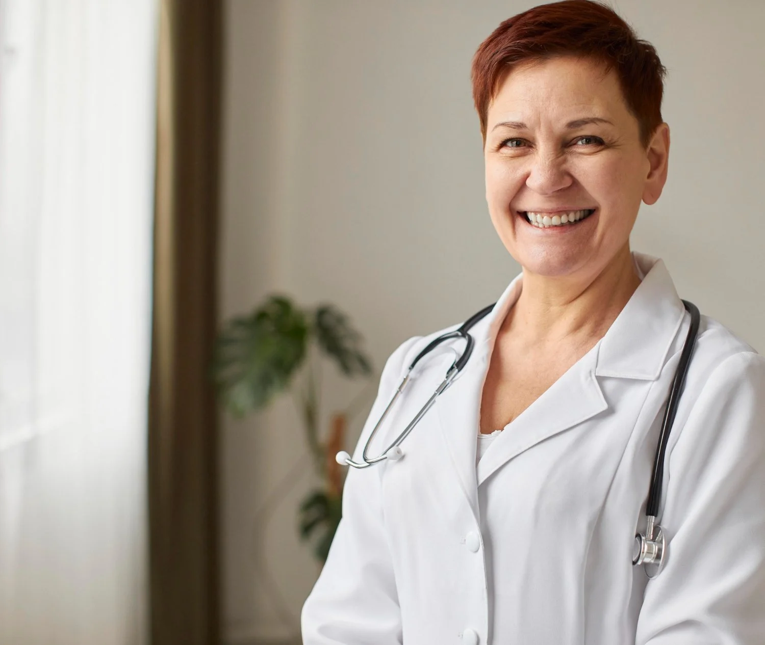 A smiling female healthcare professional wearing a white coat and a stethoscope around her neck.