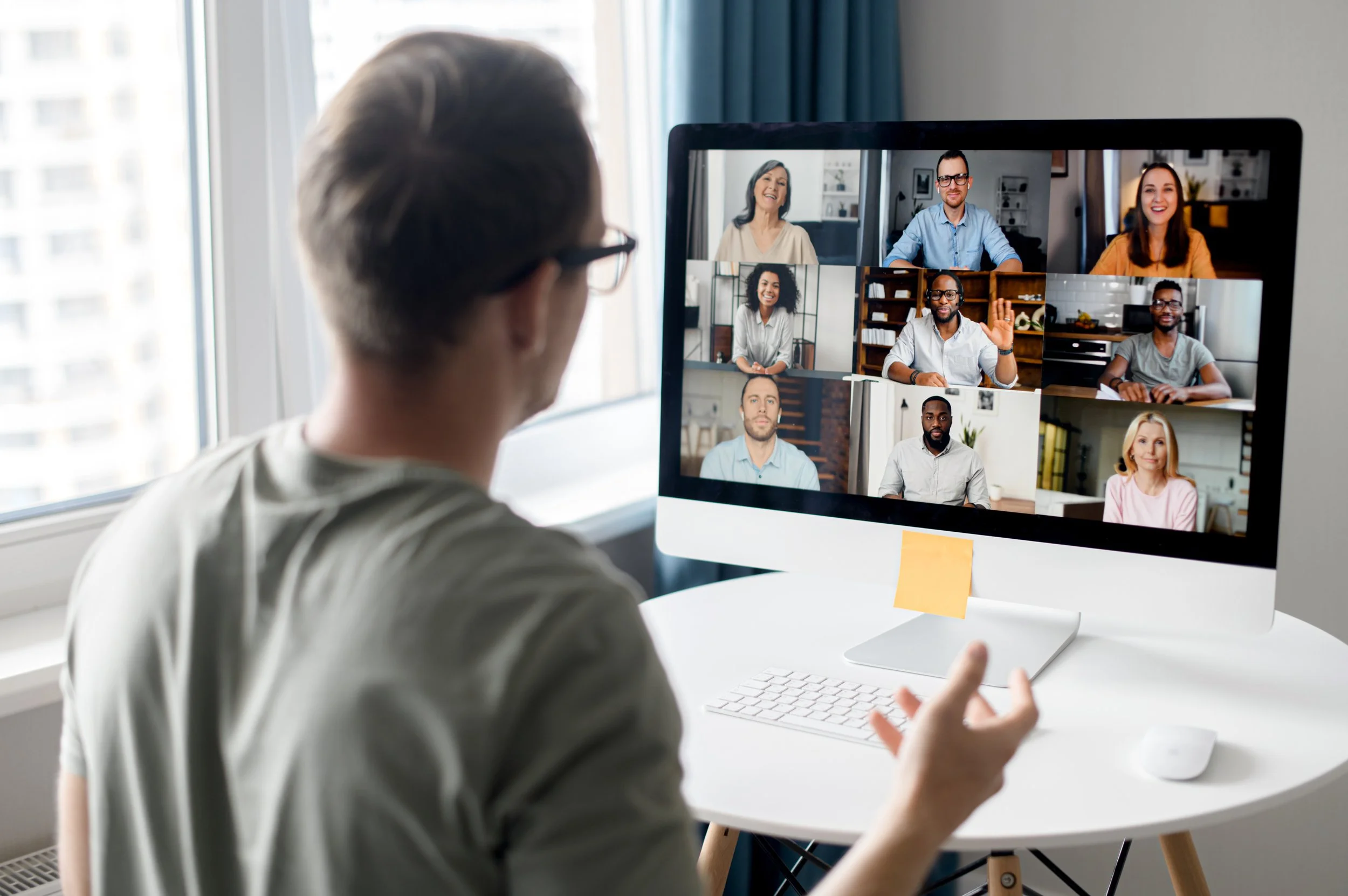 Person participating in a virtual meeting on a desktop computer with multiple people displayed on the screen