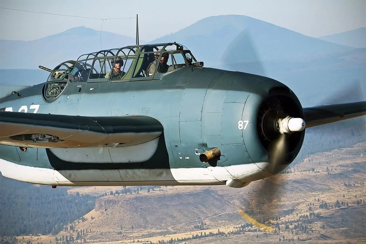 Military aircraft flying over a mountainous landscape.