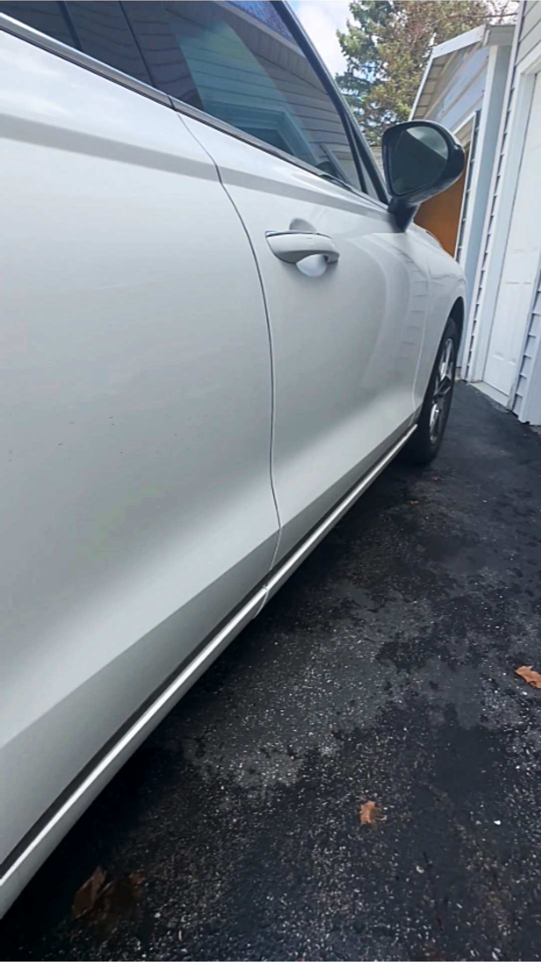 A white car parked on a driveway next to a house with white siding and a garage door.