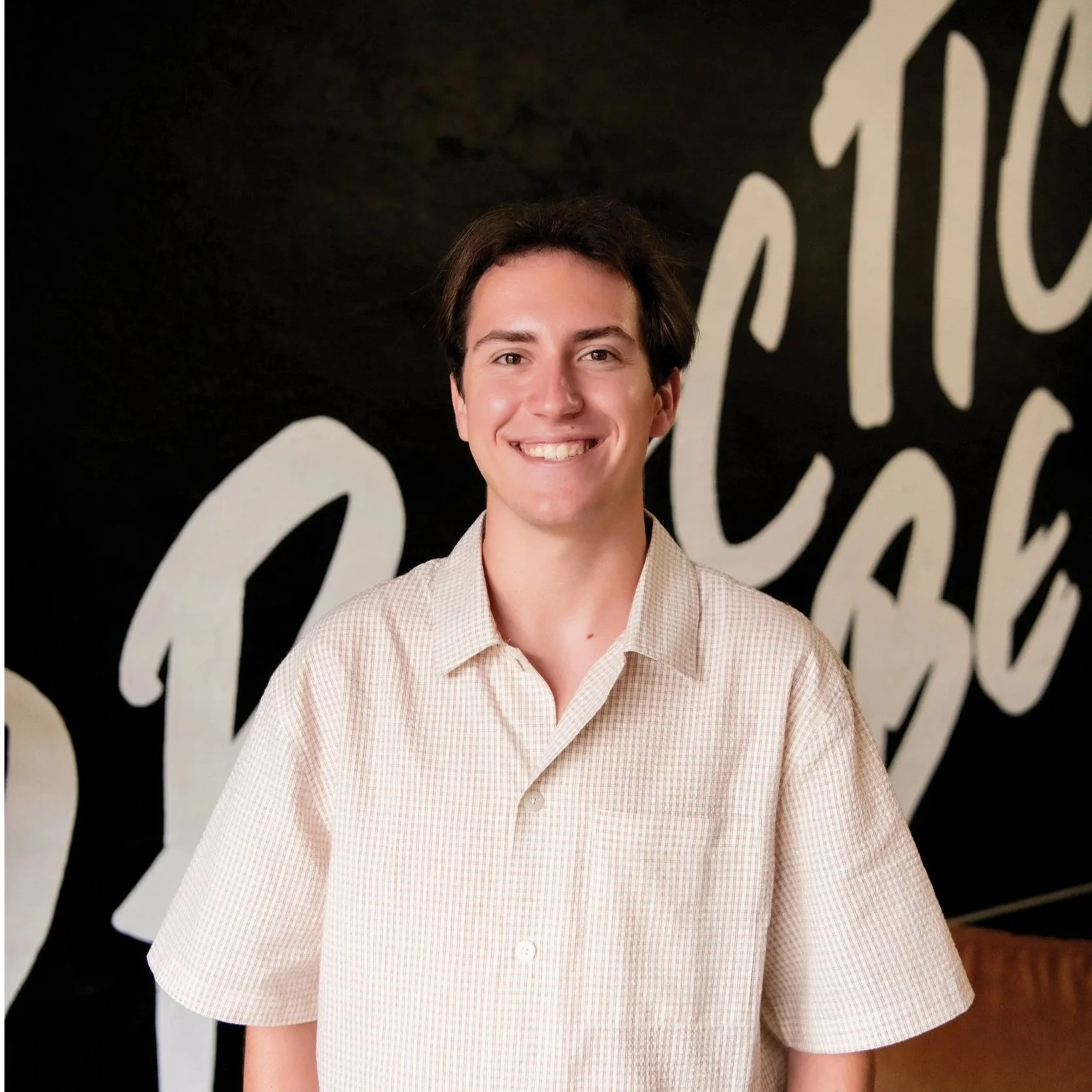 Young man with fair skin, dark hair, and a big smile, standing in front of a dark background with white cursive writing.
