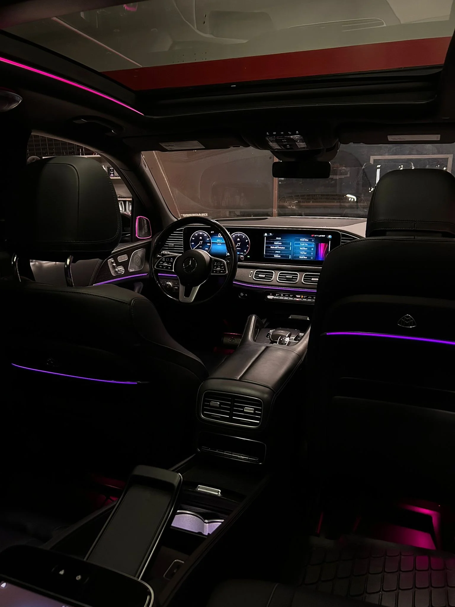 Interior view of a luxury vehicle's dashboard and front seats with ambient purple lighting, digital displays, and leather upholstery.