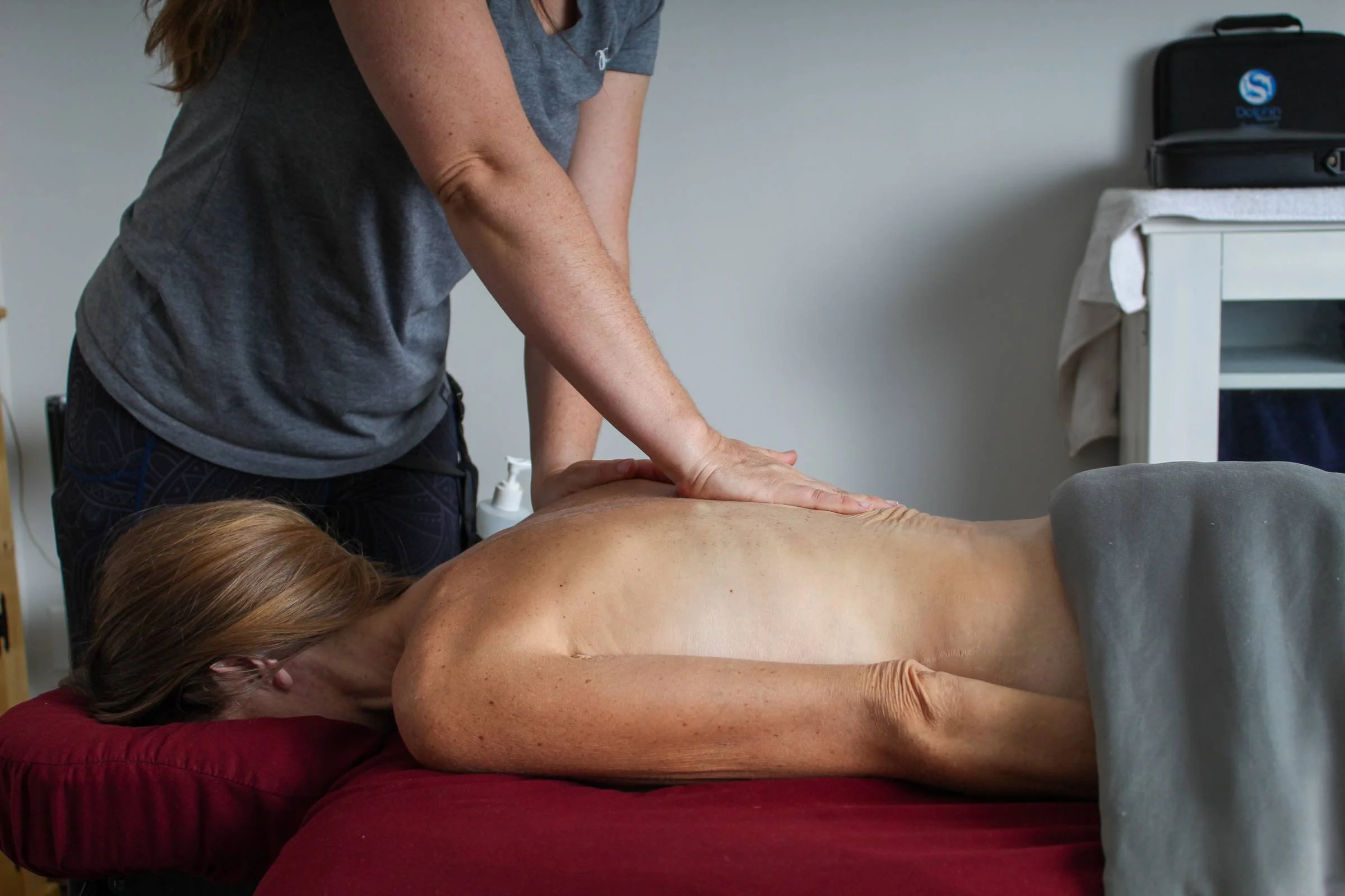 A woman receiving a massage on her back from a massage therapist in a massage room.