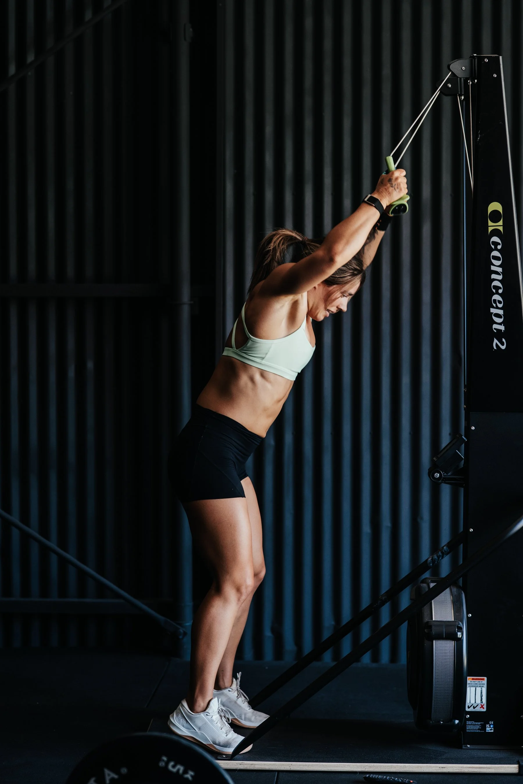 A woman exercising on a rowing machine in a gym, wearing a sports bra, shorts, and sneakers.