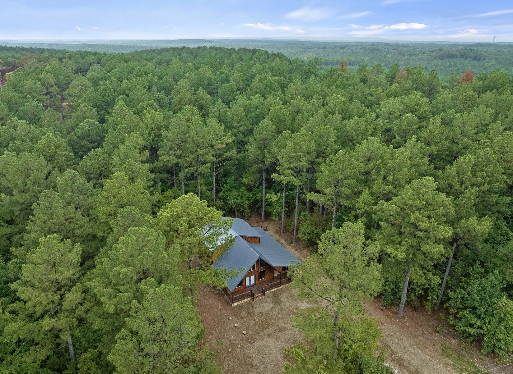 A house with a blue roof is surrounded by dense green trees in a forested area.