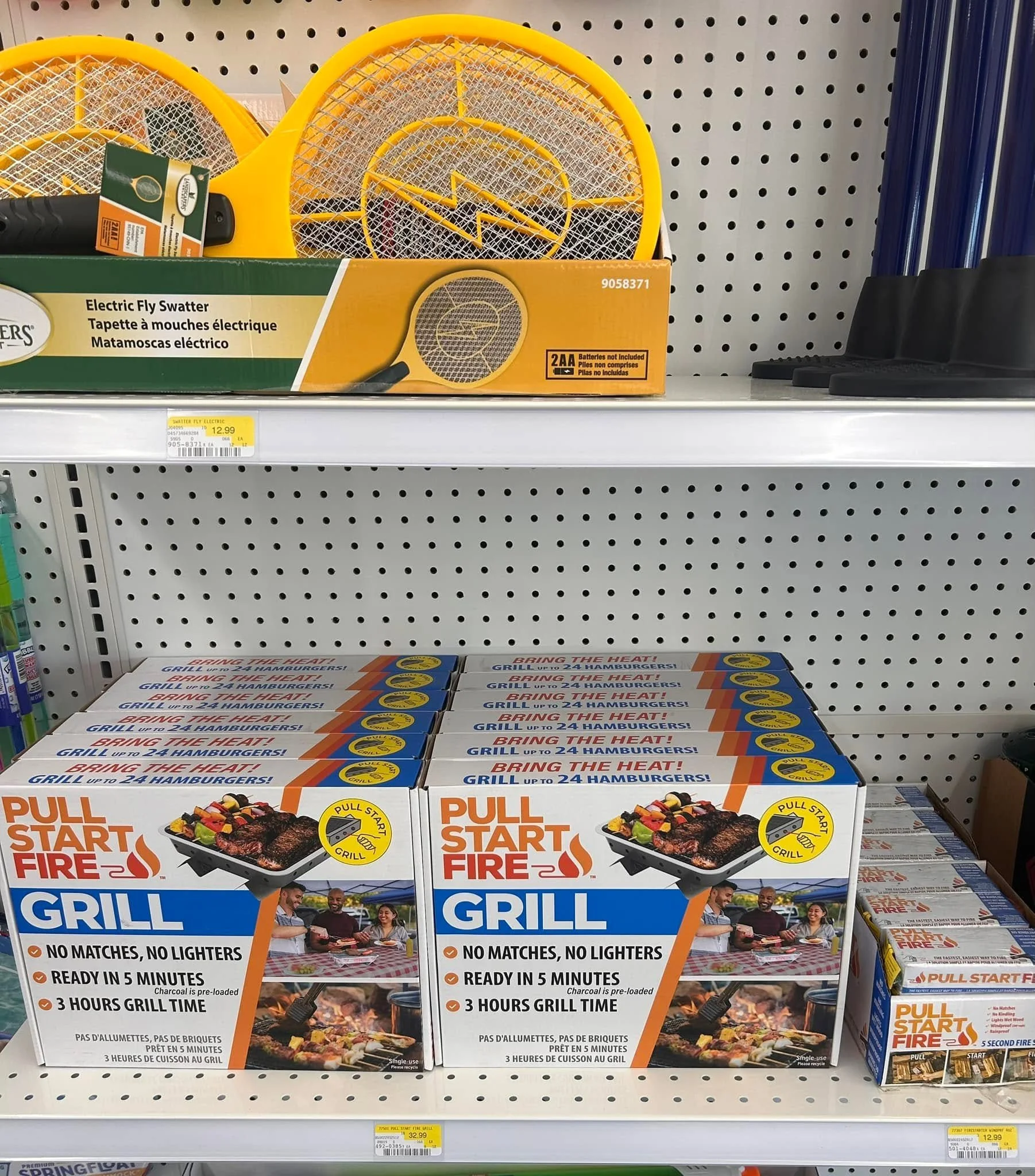 Boxes of PULL START FIRE GRILL, a self-starting charcoal grill that heats in 5 minutes with no matches or lighter needed, featuring a picture of a grill with food and people at a picnic table.